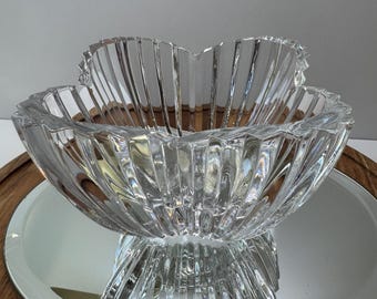 Peut inclure: Un bol en verre transparent et décoratif, avec un bord festonné et des détails verticaux côtelés. Le bol est posé sur une surface miroir, reflétant sa forme. Le design du bol rappelle une fleur.