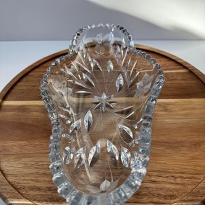 May include: A clear, decorative glass dish with a starburst and leaf design. The dish has a scalloped rim and is set on a wooden tray. The glass is etched with a floral pattern, adding a touch of elegance. Ideal for serving or display.