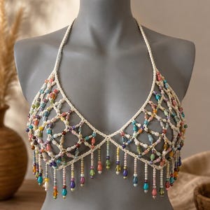 May include: A halter-style top crafted from off-white crocheted cord, featuring a geometric net pattern adorned with multicolored teardrop-shaped beads. The bottom edge is finished with a fringe of dangling beads in various hues and sizes.