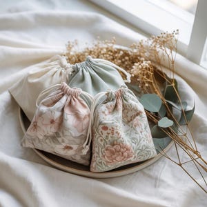 Peut inclure: Plusieurs sacs à cordon de serrage aux couleurs et motifs floraux variés. Les sacs sont disposés sur une assiette aux tons neutres, avec des fleurs séchées et de la verdure pour une esthétique naturelle. Les sacs sont en tissu et ont une fermeture à cordon.