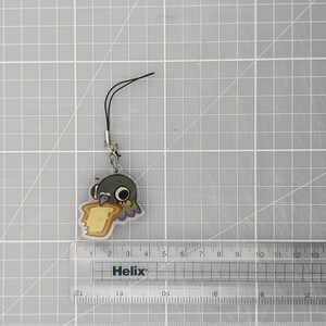 Pu&ograve; includere: Un ciondolo in acrilico trasparente con un piccione dei cartoni animati che mangia toast. Il ciondolo ha un cinturino nero e una chiusura color argento. Il piccione &egrave; grigio con collo verde e viola. Il toast &egrave; giallo e marrone.