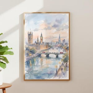 May include: A watercolour print of London, showing the Houses of Parliament, Big Ben, and the Shard. The artwork uses soft blues, oranges, and purples, framed in a wooden border. Red double-decker buses are crossing the bridges over the water.