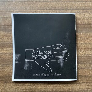 May include: Black and white image of a hand with the text "Sustainable Paper+Craft" and the website address "sustainablepapercraft.com" below.