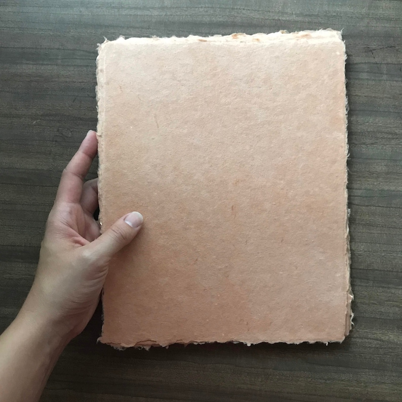 May include: A sheet of handmade paper with a textured surface and a light peach color.
