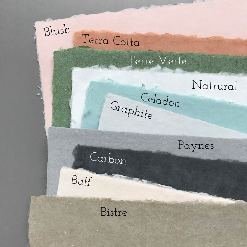 May include: A stack of paper samples in various shades of green, blue, gray, brown, and pink. The paper is textured and has a handmade look. The names of the colors are written on the paper, including Blush, Terra Cotta, Terre Verte, Natural, Celadon, Graphite, Carbon, Buff, Bistre, and Paynes.