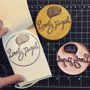 May include: Three wooden stamps with the text "hello" and "Lovely People" in a speech bubble. The stamps are on a black and white grid background.
