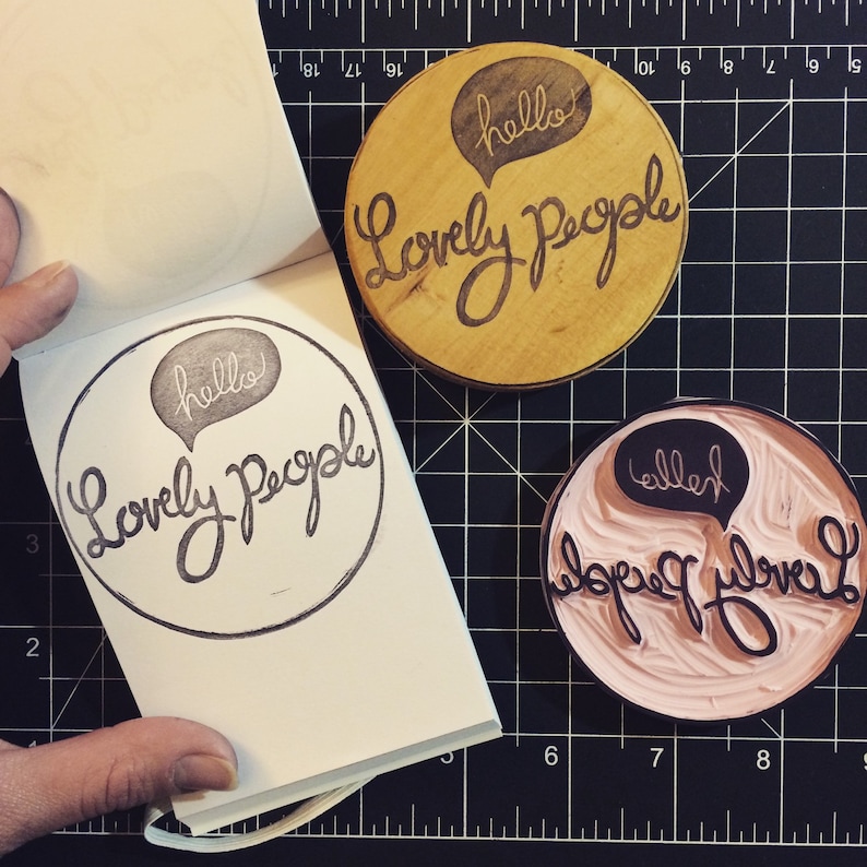 May include: Three wooden stamps with the text "hello" and "Lovely People" in a speech bubble. The stamps are on a black and white grid background.