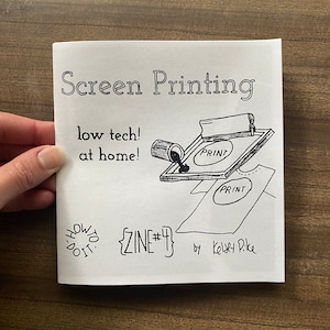 May include: A black and white illustration of a screen printing process, with the text "Screen Printing", "low tech! at home!", "PRINT", "PRINT", "{ZINE#4}", and "by Kelsey Pike".