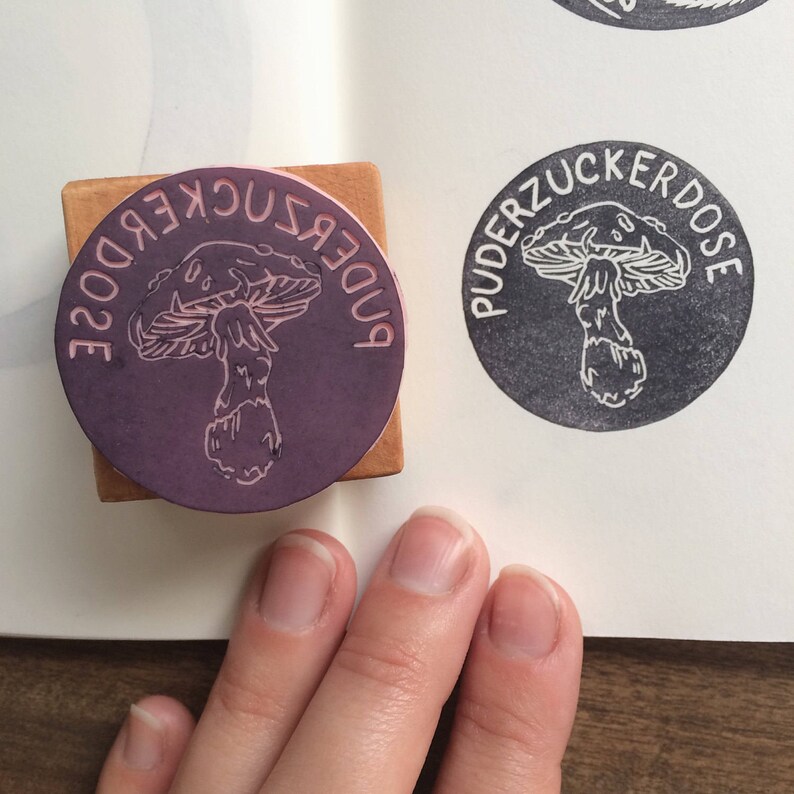 May include: A wooden stamp with a purple ink pad featuring a mushroom illustration and the text "PUDERZUCKERDOSE".