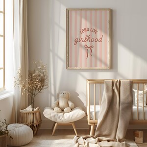 A cozy nursery with a wooden crib, a stuffed teddy bear, and a framed poster with the text "Long live girlhood" in a pink and white striped design.