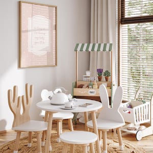 A cozy and inviting child's playroom with a white table and chairs, a small tea set, and a toy tea cart. The room has a warm and cheerful atmosphere, with a large window providing natural light and a framed picture on the wall.