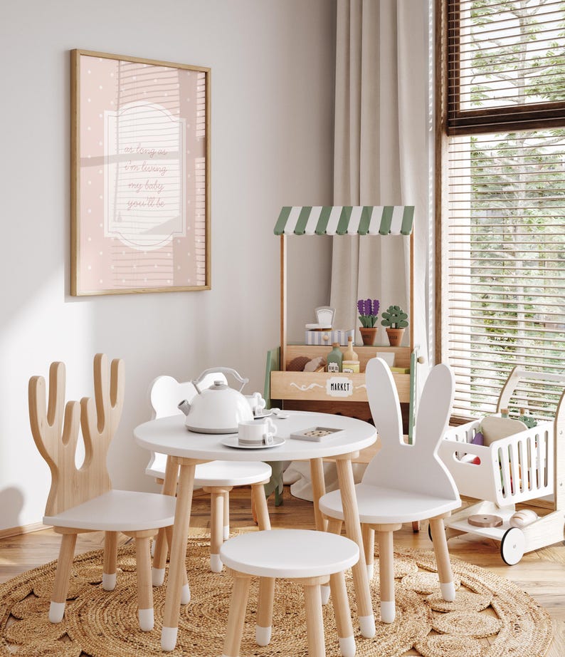 A cozy and inviting child's playroom with a white table and chairs, a small tea set, and a toy tea cart. The room has a warm and cheerful atmosphere, with a large window providing natural light and a framed picture on the wall.