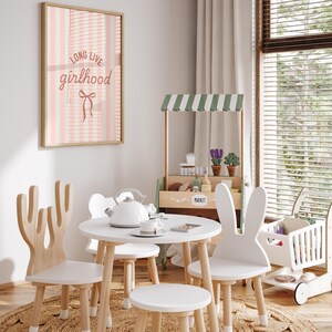 A cozy and inviting children's playroom with a pink and white striped wall hanging, a wooden play stand with a green and white striped awning, and a small table with a teapot and cups.