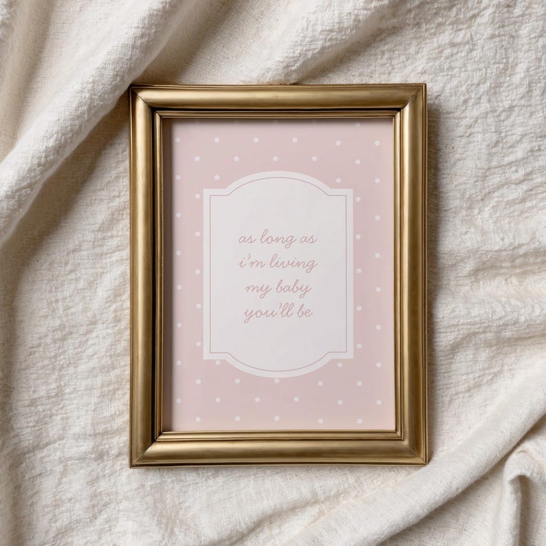 a gold-framed picture with a pink background and white polka dots, placed on a white cloth.