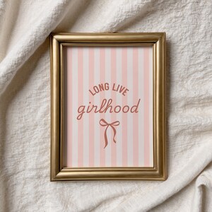 A framed picture with the text "LONG LIVE GIRLHOOD" on it, placed on a white cloth background.