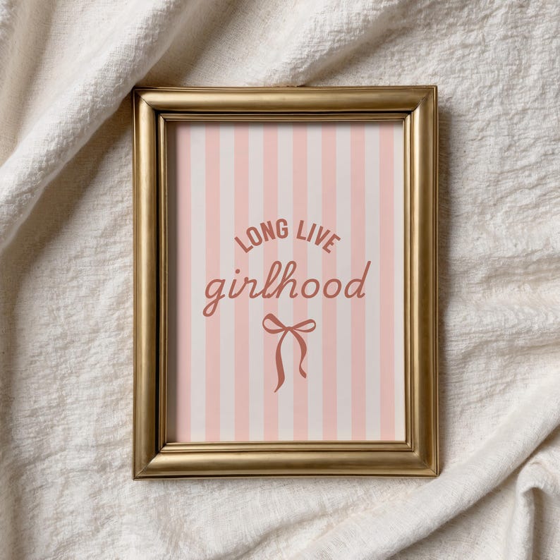 A framed picture with the text "LONG LIVE GIRLHOOD" on it, placed on a white cloth background.