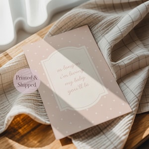 A printed and shipped card with a pink background and white polka dots, resting on a wooden surface.
