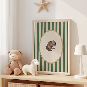 Op de afbeelding: Een ingelijste print met een illustratie van een bever in een ovale lijst met een geschulpte rand, tegen een groen-witte gestreepte achtergrond. Een teddybeer en een knuffel schaap staan op een houten plank. Onderdeel van een kinderkamerthema.