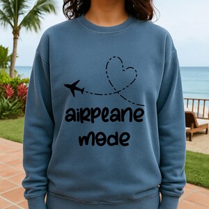 May include: A blue sweatshirt with a black airplane graphic and the words "airplane mode." The airplane's flight path forms a heart shape. The sweatshirt is a solid color and has a crew neck.