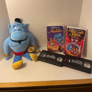 Lote coleccionable de 3 artículos de Disney "Aladdin": incluye un muñeco Scentsy Genie Buddy de 40 cm de altura sin caja ni paquete de fragancia, una cinta VHS de Aladdin y una cinta VHS de El regreso de Jafar.