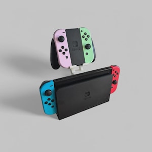 May include: A black Nintendo Switch dock with attached blue and red Joy-Cons. Above, a pair of pink and green Joy-Cons are mounted on a white stand. The Nintendo Switch logo is visible on the dock and Joy-Cons.