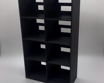 Könnte beinhalten: Schwarzes Bücherregal mit acht Fächern und rechteckiger Form. Die Regale sind gleichmäßig angeordnet. Das Design umfasst rechteckige Aussparungen an den Seiten. Hergestellt aus dunklem Material.