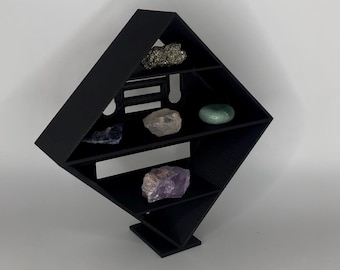 Könnte beinhalten: Schwarzes geometrisches Regal mit mehreren Ebenen, das verschiedene Kristalle und Steine präsentiert. Das Regal ist abgewinkelt und hat ein modernes Design. Zu den Kristallen gehören Amethyst, Pyrit und andere farbige Steine. Das Regal besteht aus einem soliden schwarzen Material.
