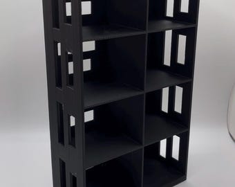 Könnte beinhalten: Ein schwarzes, rechteckiges Bücherregal mit acht Fächern. Die Seiten des Bücherregals haben rechteckige Aussparungen. Die Regale sind gleichmäßig verteilt. Das Bücherregal besteht aus einem soliden, mattschwarzen Material.