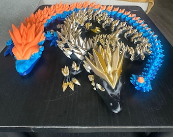 May include: Three articulated dragon sculptures in orange, blue, gold, and black. The dragons have spiky details and are posed on a dark surface. The sculptures are likely 3D printed and are a unique decorative item.
