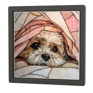 May include: A framed artwork featuring a Shih Tzu dog peeking out from under a pink and white patterned blanket. The dog has brown and white fur with dark eyes and nose. The frame is dark gray.
