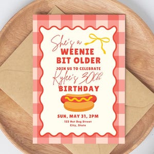 Op de afbeelding: Een rechthoekige verjaardagsuitnodiging met een rood-witte gingham rand. De tekst luidt: She's a WEENIE BIT OLDER JOIN US TO CELEBRATE Kylee's 30th BIRTHDAY SUN, MAY 31, 2PM 123 Hot Dog Street City, State. Een afbeelding van een hotdog staat centraal.