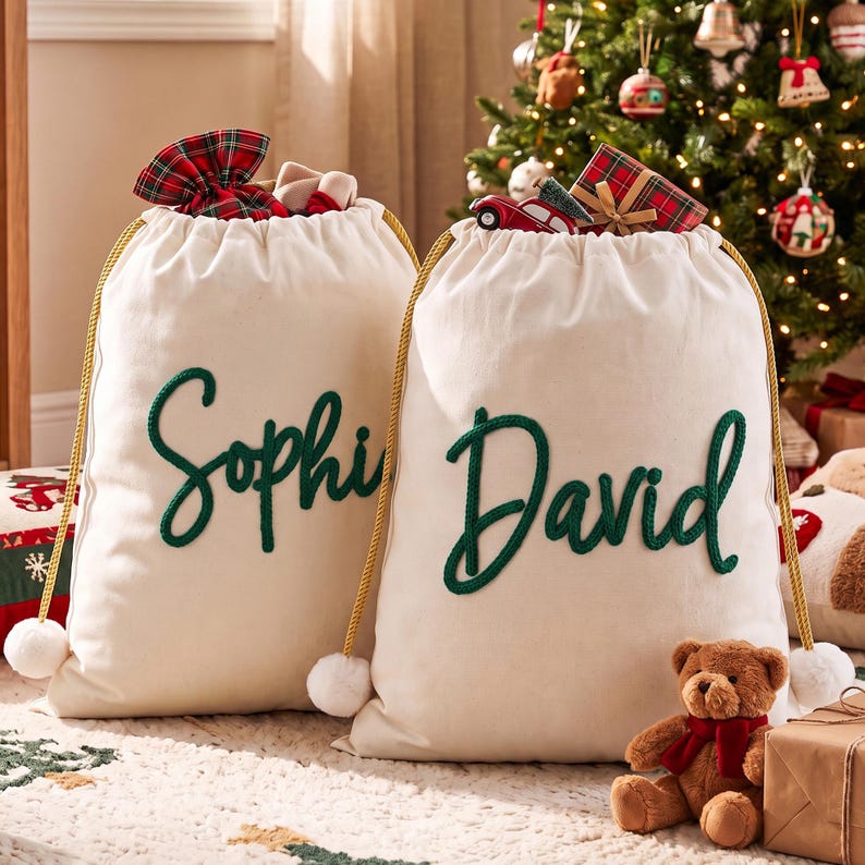 May include: Two off-white canvas drawstring bags with gold cords and white pom-poms. The left bag features the name Sophie in green cursive script, and the right bag features the name David in green cursive script, both filled with gifts.
