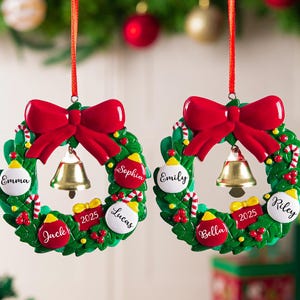 K&ouml;nnte beinhalten: Zwei kreisf&ouml;rmige Weihnachtskranz-Anh&auml;nger, die an roten B&auml;ndern h&auml;ngen. Jeder gr&uuml;ne Kranz hat eine gro&szlig;e rote Schleife oben, eine goldene Glocke in der Mitte und kleine rot-wei&szlig;e Kugeln mit den Namen Emma, Sophia, Jack, Lucas, Emily, Bella und Riley sowie ein rotes Geschenk mit der Aufschrift 2025.
