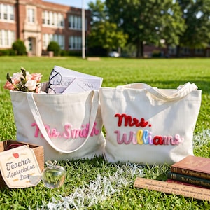 May include: Two off-white corduroy tote bags featuring personalized names in raised, colorful yarn lettering. One bag displays 'Ms. Smith' in pink, while the other shows 'Mrs. Williams' in red, pink, yellow, and blue. A wooden ruler is visible nearby.