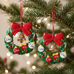 K&ouml;nnte beinhalten: Zwei kreisf&ouml;rmige Weihnachtsbaumschmuck-Kr&auml;nze mit gr&uuml;nem Blattwerk, einer gro&szlig;en roten Schleife oben und einer goldenen Glocke in der Mitte. Jeder Kranz enth&auml;lt kleine Zuckerstangen, rote Beeren und Kugeln, die mit Namen und 2026 beschriftet sind.
