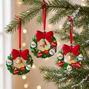 K&ouml;nnte beinhalten: Drei kreisf&ouml;rmige Weihnachtskranz-Ornamente, die an roten B&auml;ndern h&auml;ngen. Jeder gr&uuml;ne Kranz ist mit einer gro&szlig;en roten Schleife, einer goldenen Glocke und kleinen bunten Kugeln mit Namen wie Lucas, Emma, Harper, Mom, Dad, Sophia, Liam, Chloe, Anna, Jack, Emily und Asher sowie der Jahreszahl 2026 versehen.