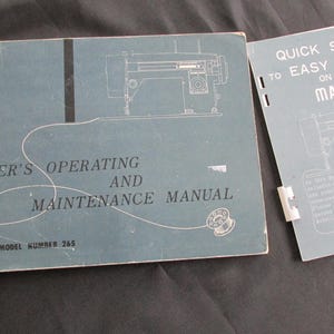 Peut inclure: Un manuel de machine à coudre bleu avec le titre "Owner's Operating and Maintenance Manual" et le numéro de modèle 265. Une brochure bleue séparée intitulée "Quick Steps to Easy Sewing on Your Machine" est également visible.