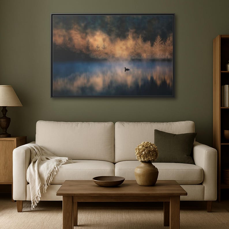 May include: A framed landscape art print depicts a serene lake scene. The artwork features a misty atmosphere with a duck on the water, and the reflection of trees. The color palette includes blues, oranges, and greens, creating a tranquil ambiance.