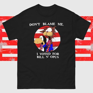 May include: Black t-shirt with a cartoon graphic of two characters inside a red and white circle. The text reads "DON'T BLAME ME, I VOTED FOR BILL N' OPUS."