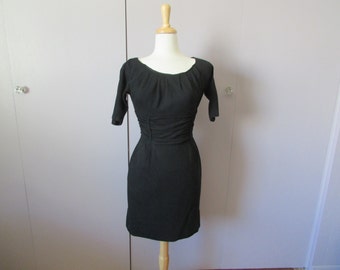 May include: A black, short-sleeved dress with a fitted bodice and a slightly flared skirt. The dress has a scoop neckline and a gathered detail at the waist.