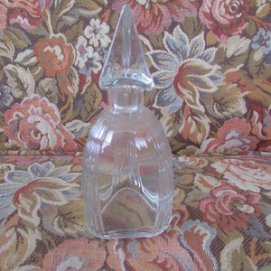 Peut inclure: Flacon de parfum en verre transparent avec un bouchon pointu. La bouteille présente des détails verticaux côtelés et une base arrondie. Le bouchon est de forme claire et pointue. Il s'agit probablement d'un article décoratif vintage.