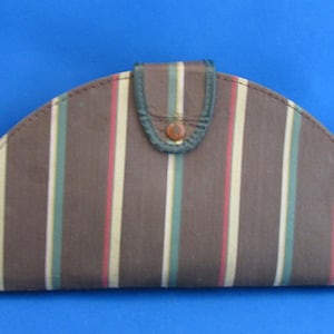 Może przedstawiać: Brązowe, półksiężycowate etui z pionowymi paskami w kolorze czerwonym, zielonym i kremowym. Etui posiada zapięcie na klapę z małym, okrągłym guzikiem. Krawędzie są obszyte na zielono.