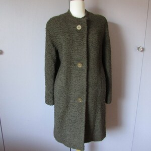 Peut inclure: Un manteau long à manches longues, de couleur vert olive, texturé, avec un col montant et trois boutons dorés.