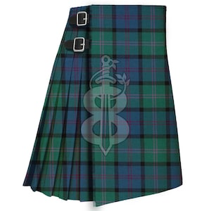 Könnte beinhalten: Ein grüner, blauer und schwarzer Schottenkilt mit zwei schwarzen Lederriemen und silbernen Schnallen. Der Kilt hat ein plissiertes Design und ein dekoratives Emblem. Gewebter Stoff.