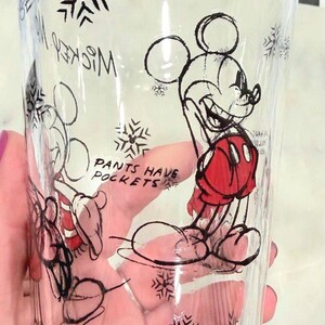 Pu&ograve; includere: Bicchiere trasparente con un disegno di Mickey Mouse nero e rosso, con motivi a fiocco di neve. Il testo "Pants Have Pockets" &egrave; visibile. Il bicchiere &egrave; cilindrico e sembra essere un bicchiere da bere.