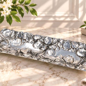 May include: A rectangular silver-toned metal tray featuring a raised, textured relief pattern of numerous apples and leaves covering the entire border and edges, with a smooth, reflective central surface for display.