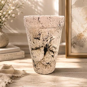May include: A tapered, off-white planter with a textured, crackled finish and a prominent, raised relief of a butterfly on the front. The surface features dark, weathered veining throughout, creating a distressed appearance on the exterior.