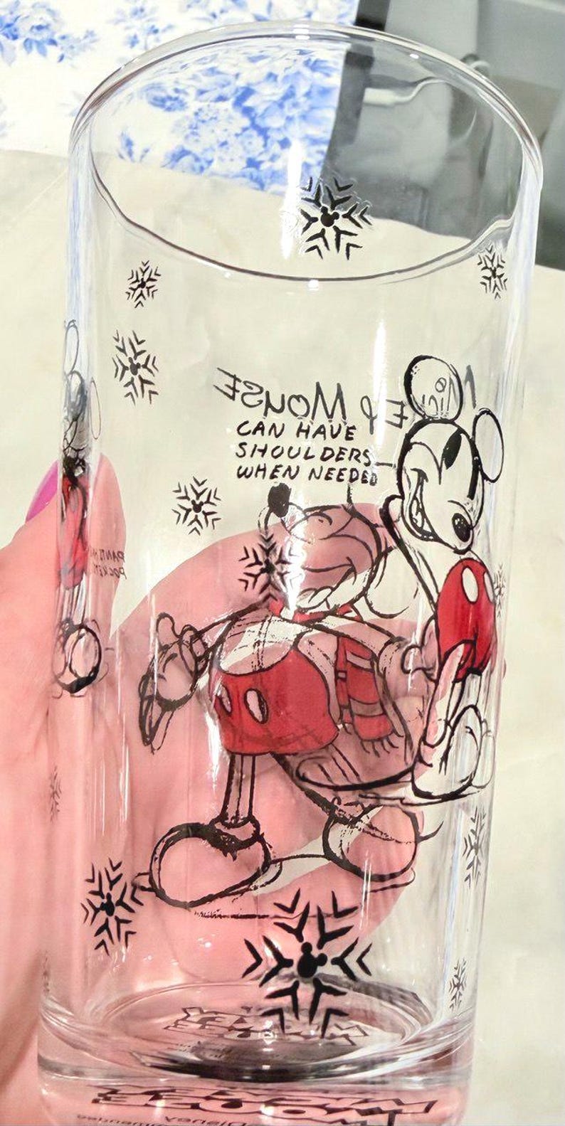 Pu&ograve; includere: Bicchiere di vetro trasparente con un'illustrazione di Topolino in nero, rosso e bianco. Il design include fiocchi di neve e il testo "Mickey can have shoulders when needed". Un bicchiere decorativo.