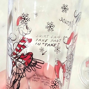 Pu&ograve; includere: Bicchiere trasparente con un'illustrazione di un personaggio dei cartoni animati in abito rosso e bianco, con fiocchi di neve e testo. Il testo recita "SKIRT CAN TAKE PART IN TAKE".