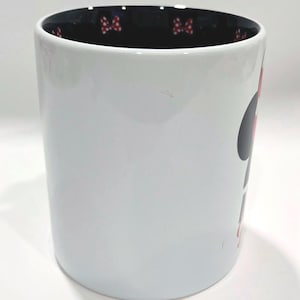 Puede incluir: Taza de cer&aacute;mica blanca con dise&ntilde;o de Minnie Mouse. La taza tiene un interior negro con detalles de lazo rojo. Una gran silueta de Minnie Mouse est&aacute; en el lateral.